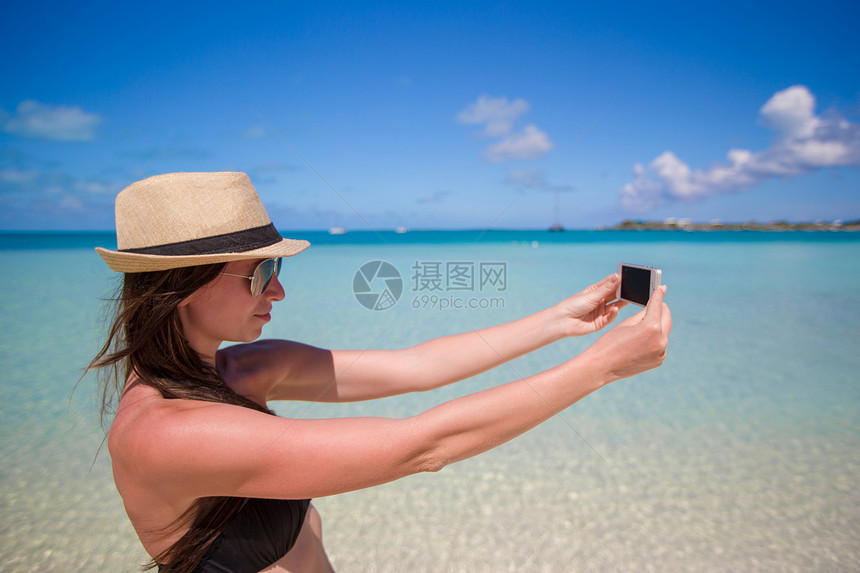 年轻女子在热带海滩的手机上拍照照片漫游细胞友谊幸福消息女士女性乐趣海洋图片