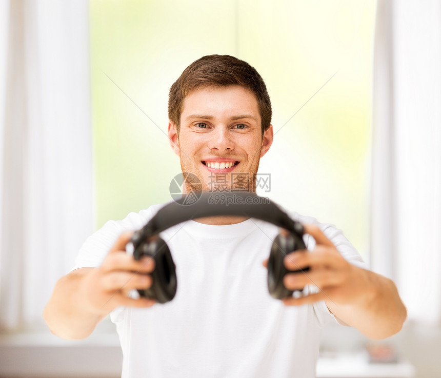 年轻微笑的男子在家里提供耳机图片