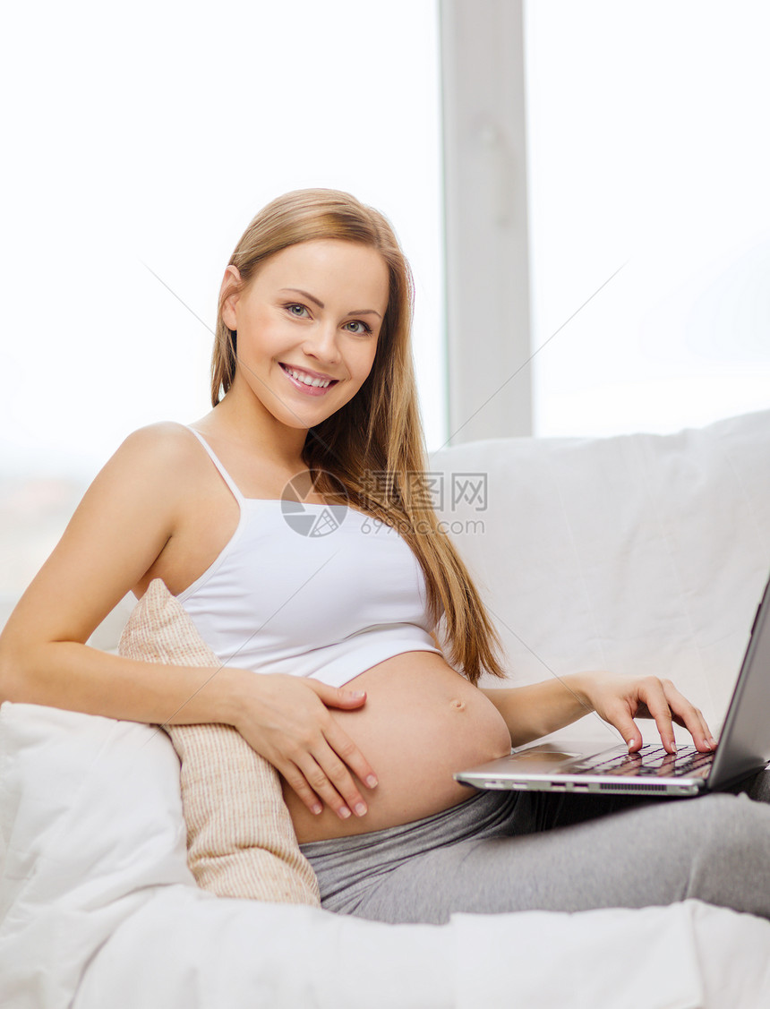 带笔记本电脑 微笑着的孕妇女性技术母性说谎肚子互联网婴儿父母腹部沙发图片
