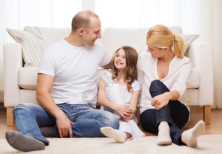 坐在地毯父母和小女孩坐在家中的地板上女士幸福母亲爸爸地面女儿孩子拥抱男人房间背景