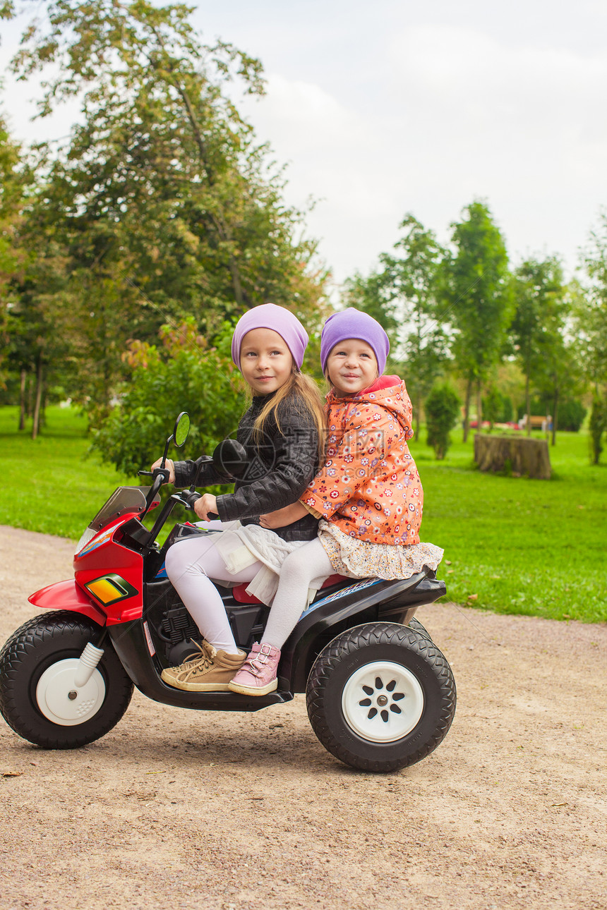 可爱的小女孩 在绿色公园骑着孩子的摩托车微笑运输玩具游戏夹克自行车引擎喜悦速度运动图片