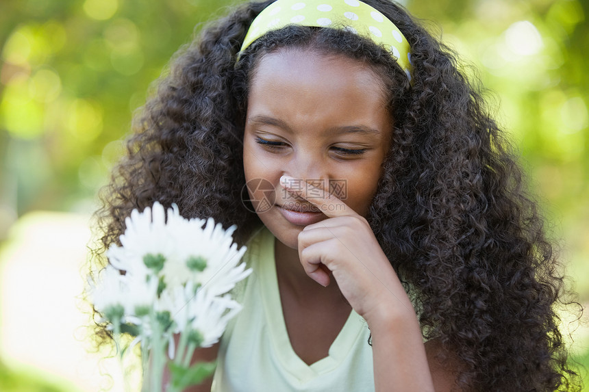 年轻女孩拿着花朵 在公园中遮住鼻子图片