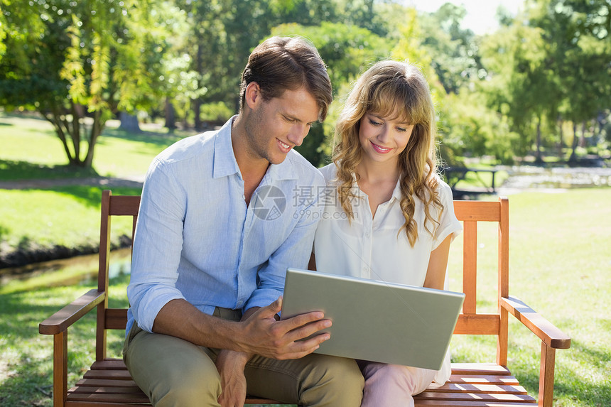 坐在公园长椅上看笔记本电脑的一对可爱情侣夫妻男人太阳阳光女朋友女性绿地女士技术衬衫图片