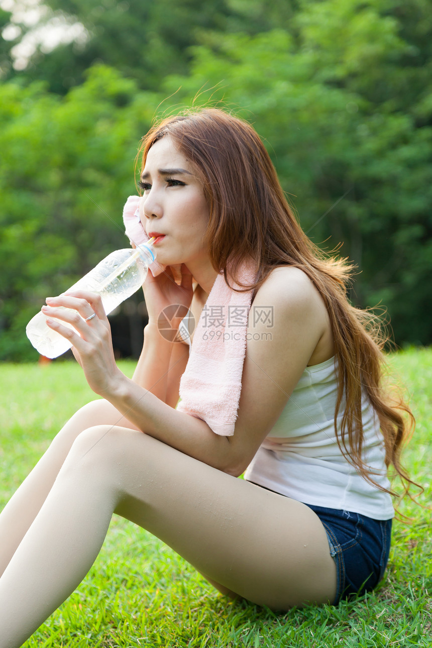 妇女在锻炼后坐着疲劳和饮用水女性瓶子女士公园女孩身体毛巾草地运动成人图片