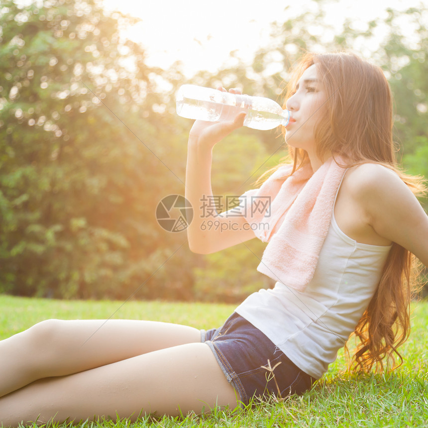 妇女在锻炼后坐着疲劳和饮用水运动日落女孩身体阳光女性公园女士草地瓶子图片