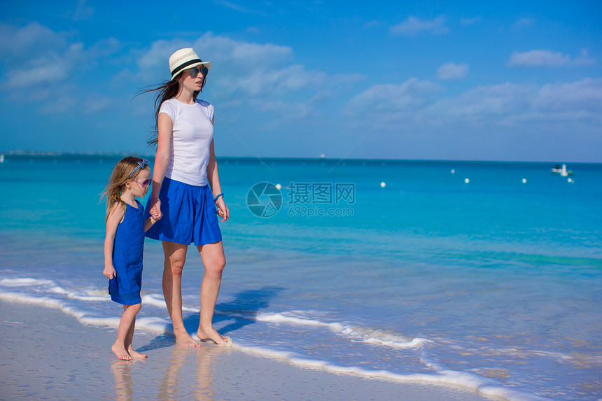 母亲和女儿在热带沙滩上走着海岸线父母女性帽子海岸孩子女士乐趣童年父亲图片