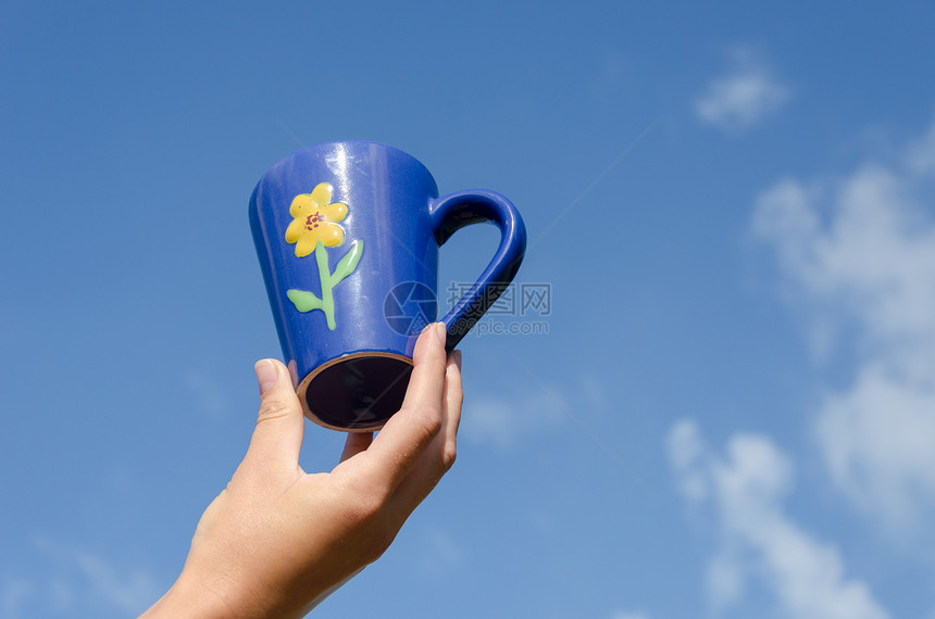 手握蓝色粘土杯花朵 蓝蓝天空背景图片