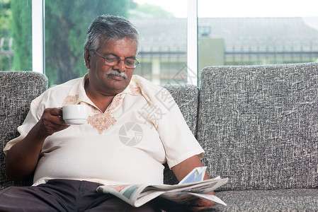 印度高龄成人在读新闻报时喝咖啡背景图片