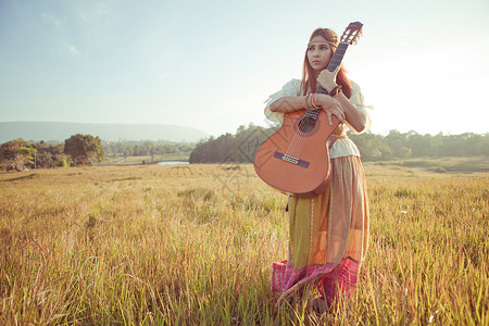 在金田中行走的嬉皮妇女场地吉他手自由女性吉他国家女士草地女孩青少年背景图片