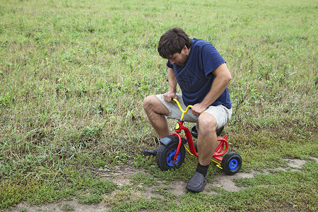 不忘童心成人男子骑小三轮车玩具深色骑术困惑乐趣姿势农村男性童心男人背景