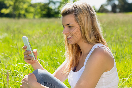 金发美女坐在草地上 送短信女性长发牛仔布头发微笑快乐农村阳光环境闲暇背景图片