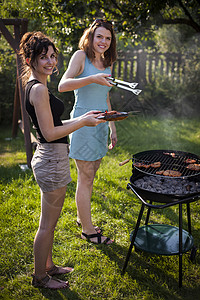 两个漂亮女孩在烤架上做饭花园火焰香肠饮食牛扒木炭女性炙烤烹饪烧伤背景图片