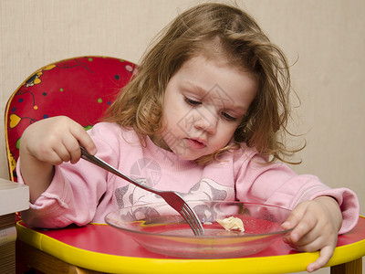 坐着吃饭的女孩两岁的女孩在厨房餐桌上用叉子吃饭早餐盘子热情桌子食物午餐背景