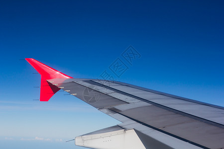 机翼飞机在云上飞翔 从西向天空仰望红色引擎蓝色窗户喷射技术旅行运输翅膀白色背景