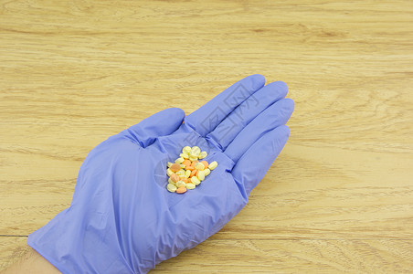 手戴紫色乳胶手套 装有黄和橘子药丸背景图片