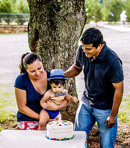 拉丁裔家庭与婴儿生日蛋糕孩子生日帽子领结蛋糕蓝色背景图片