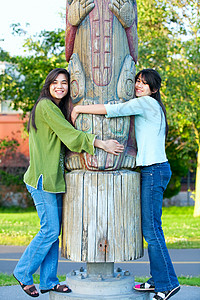 少数民族图腾两个年轻 两种族的少女 在公园抱抱一个图腾柱背景
