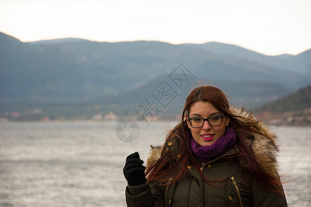 参加冬季游览的年轻女孩旅行兜帽夹克眼镜围巾紫色山脉背景图片