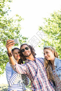 快乐的朋友自拍潮人绿地照片手机社交男性太阳镜阳光女性公园背景图片