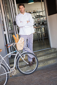 面包店门口手交叉和骑自行车的微笑面包师背景