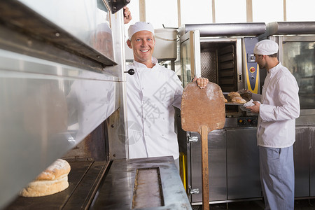快乐的面包师微笑在相机上烤箱合作白人厨房餐厅同事饮食职业男人大楼背景图片