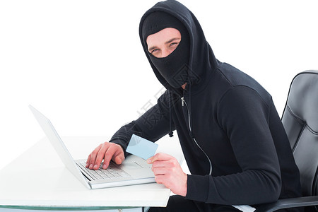 使用笔记本电脑和信用卡的黑客技术男性兜帽电子商务身份骇客桌子网站网络办公椅背景图片