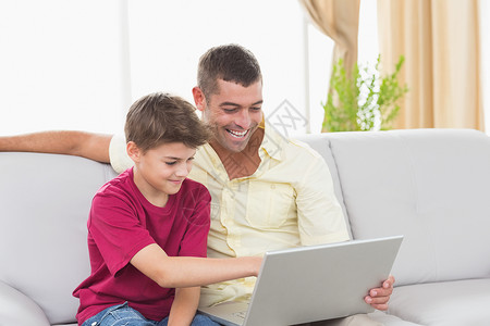 父亲和儿子在沙发上使用笔记本电脑男生技术孩子成人快乐家庭客厅男性休息室男人背景图片