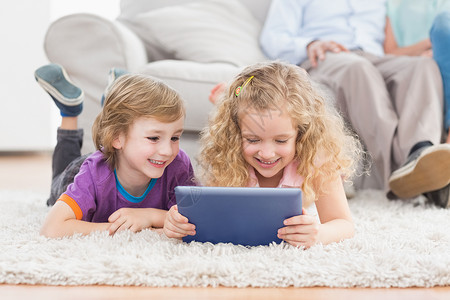 哥哥和姐姐在地毯上使用数字平板电脑图片