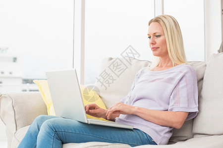 在沙发上使用笔记本电脑的妇女金发女性家庭生活长椅闲暇女士金发女郎软垫成人浅色背景图片