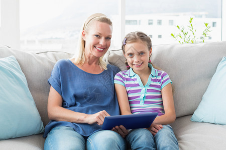 幸福的母亲和女儿在沙发上使用数字平板电脑背景图片