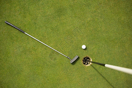 推杆果岭高尔夫球俱乐部和高尔夫球在旗边加绿色阳光时间球场爱好闲暇运动活动晴天旗帜假期背景
