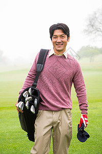 高尔夫袋Golfer站在镜头前笑着拿着高尔夫球袋毛衣手套活动背心多云服装爱好云端微笑高尔夫背景