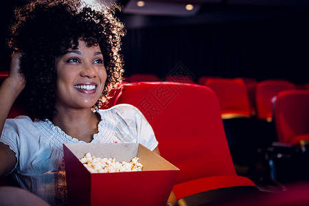 微笑的年轻女子在看电影文艺演出礼堂闲暇电影院爆米花电影红色椅子混血背景图片