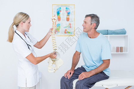 医生向病人展示解剖脊椎女士颈椎讨论疝气治疗痛苦疾病压力女性按摩师背景图片
