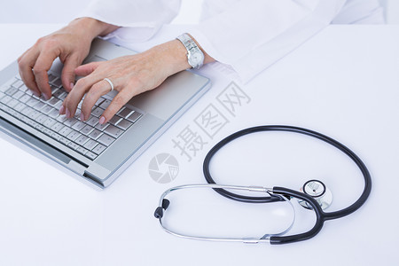 在笔记本电脑上工作的医生服务医疗女性从业者工作服专注桌子技术实验专家背景图片
