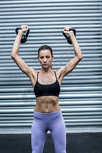 推举一个肌肉女人举着小叮当专注俱乐部运动员护理中心重量身体训练健身健身房背景
