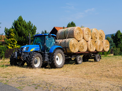 蓝色马车收获季节的拖拉机和装满干草堆的马车背景