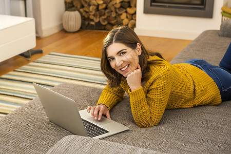 利用手提笔记本电脑工作的妇女女士房间长椅技术沙发学习房子微笑互联网背景图片