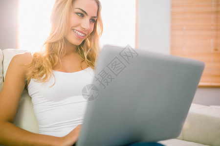 在沙发上用笔记本电脑浅色家庭生活女士工作室公寓住所闲暇微笑女性金发女郎背景图片