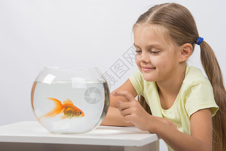 快乐的小女孩 用金鱼在水族馆上敲他的手指高清图片