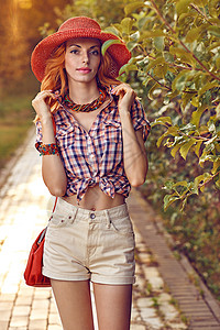 美女红发女人在公园 户外微笑女孩调子短裤背景享受花园日落花朵帽子衬衫背景图片
