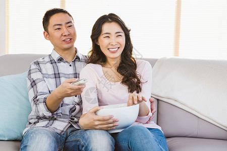 坐在沙发上快乐的情侣微笑手表爆米花女朋友情人饮食夫妻女性情怀食物背景图片