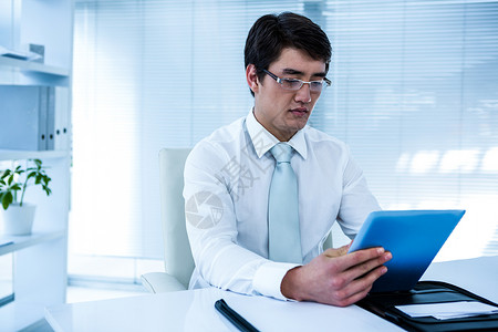严重的亚洲商务人士使用他的平板电脑男生药片领带套装滚动旋转椅眼镜男性办公室职业背景图片