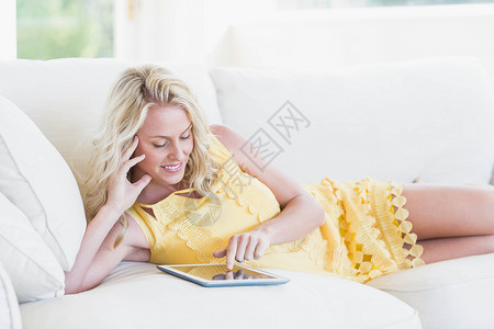 快乐的女人在沙发上用石板成人触摸屏枕头闲暇女性客厅头发电脑家庭生活软垫背景图片