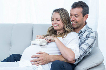 坐在沙发上的怀孕夫妇男性拥抱客厅房子快乐女性腹部肚子孕妇装公寓背景图片