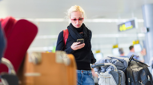 女性旅行者在机场等候时使用手机进行等待时间上网女孩通勤者互联网公共汽车大堂飞机场游客女士背景