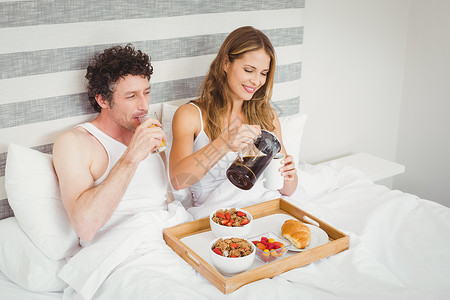 在床上吃早餐的一对微笑的夫妇高清图片