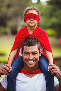 英雄贴穿着超级英雄服装的女孩 坐在父亲肩上混血面具俏皮微笑快乐英雄女儿喜悦男人男性背景