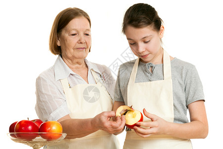 外祖母教孙女切除皮的皮毛孩子祖父母围裙祖母食物女孩厨房微笑白色红色背景图片