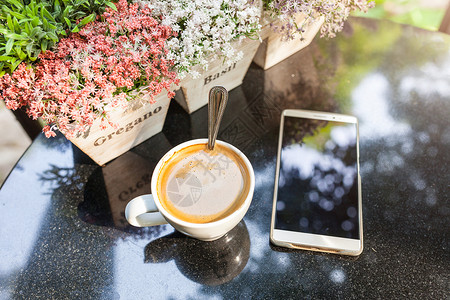数字智能手机和桌上的咖啡杯 配有古花餐厅阳光动机茶点想像力店铺潮人咖啡店拿铁战略背景图片